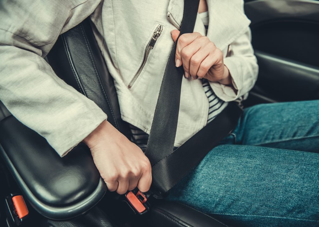 Cropped image of girl fastening a seat belt while driving a car - Seat Belt Law